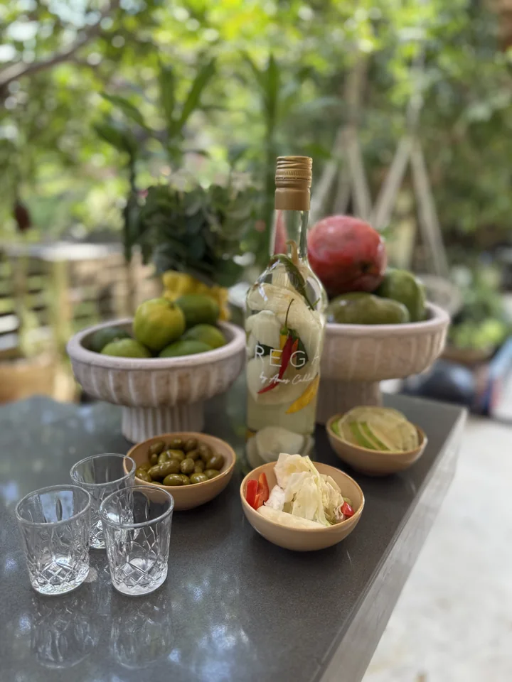 A REGA bottle containing cut fruit and red pepper, beside olives and glasses