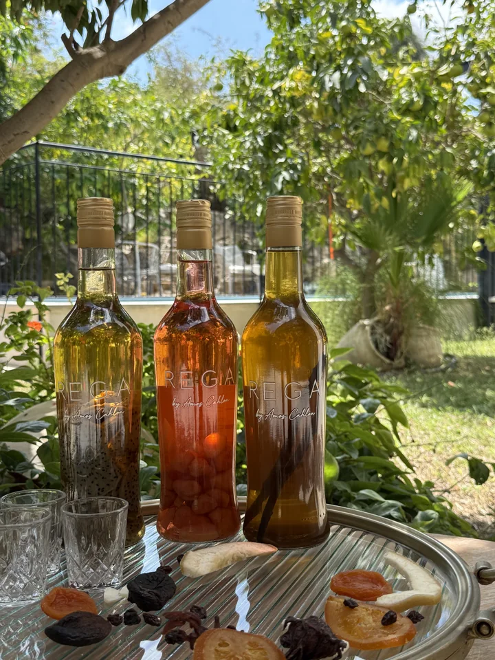 Three REGA bottles on a silver tray in the garden, with glasses and fruit