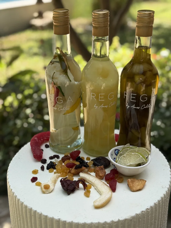 Three REGA bottles on a white table with fruit, spices and serving dishes