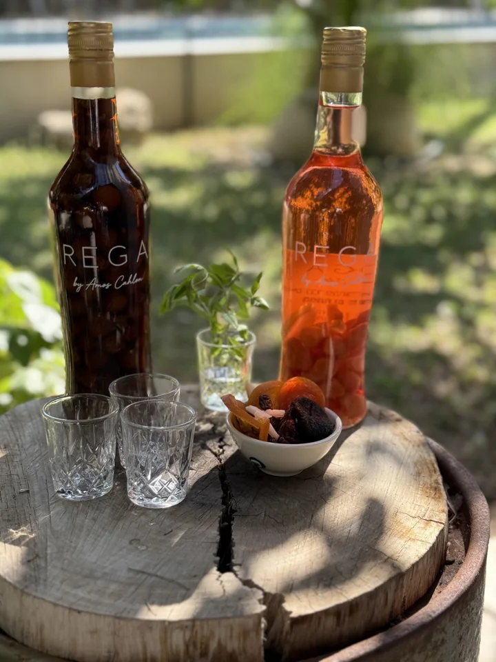 Two red and amber REGA bottles on a wooden surface beside glasses